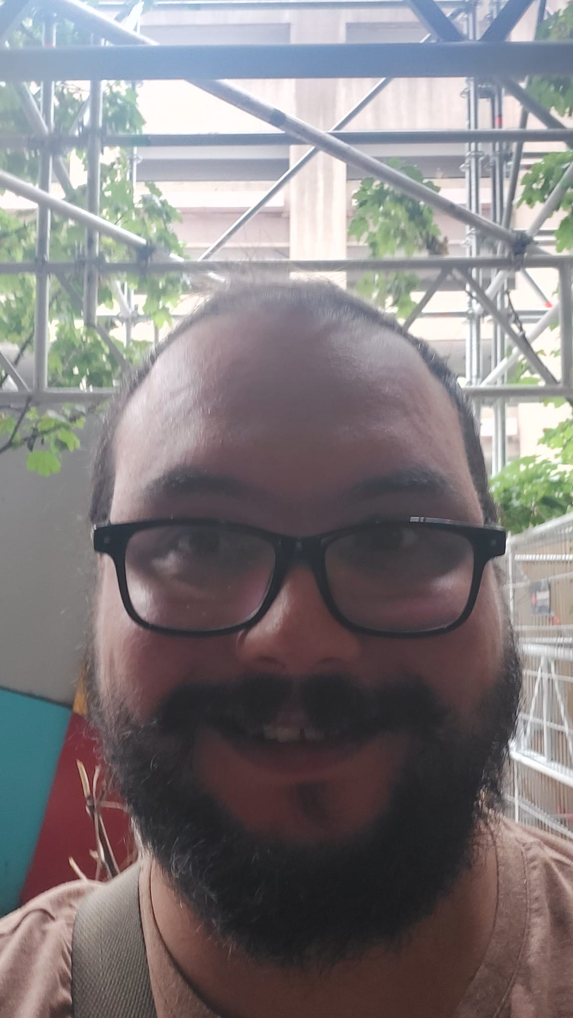 A man short hair and bushy facial hair stands in front of construction scaffolding looking forward